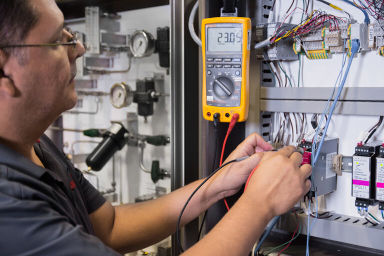 Technician using a multimeter to verify electrical signals in a process analyzer control panel